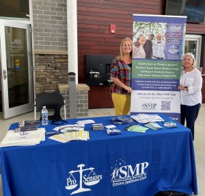 Display table with brochures, two women standing beside informational banner about Ohio Senior Medicare Patrol.
